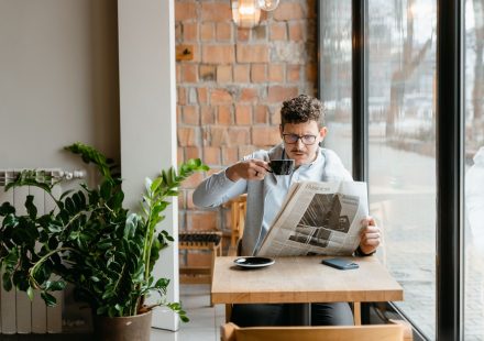 Man sitting indoors with coffee and newspaper, surrounded by plants by the window. — Auf welche Spiele sind die Kunden in Slo