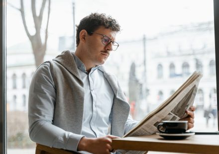 Adult man reads a newspaper by a café window, enjoying a coffee break indoors. — God of Coins Casino: Ein Blick hinter die Ku