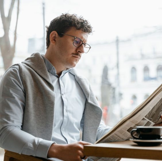 Adult man reads a newspaper by a café window, enjoying a coffee break indoors. — God of Coins Casino: Ein Blick hinter die Ku