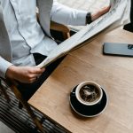 An adult male enjoying his coffee while reading a newspaper at a cafe with his smartphone nearby. — Le profil complet de Loco