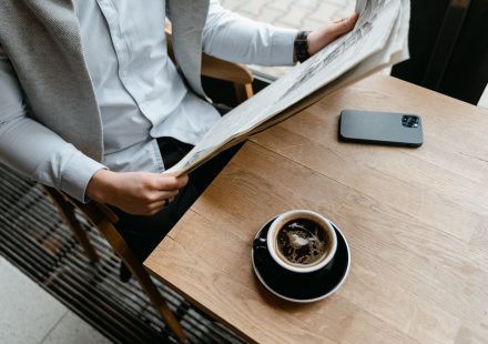 An adult male enjoying his coffee while reading a newspaper at a cafe with his smartphone nearby. — Le profil complet de Loco