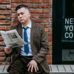 A professional man in formal wear reads a newspaper beside a coffee shop window. — test123123