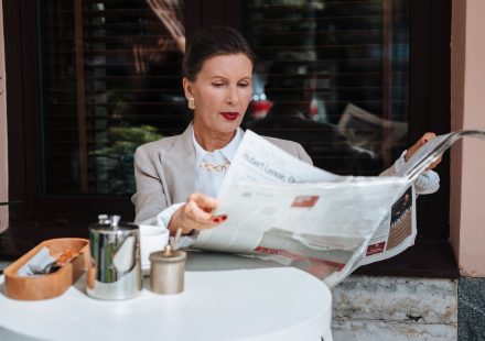 Sophisticated woman enjoying her morning newspaper at a cozy outdoor cafe. — Warum Instant Casino bei Spielern immer beliebte