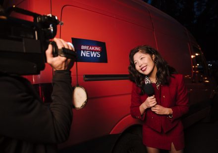 Asian female reporter in a red blazer reporting live on the news outdoors in the evening. — Wie attraktiv sind die VIP-Progra