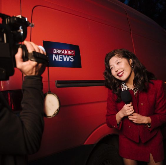 Asian female reporter in a red blazer reporting live on the news outdoors in the evening. — Wie attraktiv sind die VIP-Progra