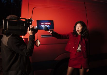 Asian female reporter with cameraman conducting a nighttime news broadcast beside a news van. — Wie schnell sind die Auszahlu